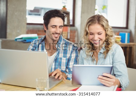 Smiling colleagues working on technology while sitting in office