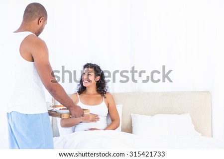 Husband serving breakfast for happy pregnant wife on bed at home