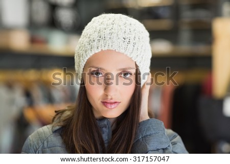 Serious pretty brunette looking at camera with winter clothes in clothes store