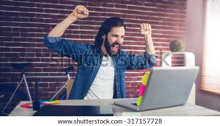 Cheerful creative businessman with arms raised looking at laptop in office