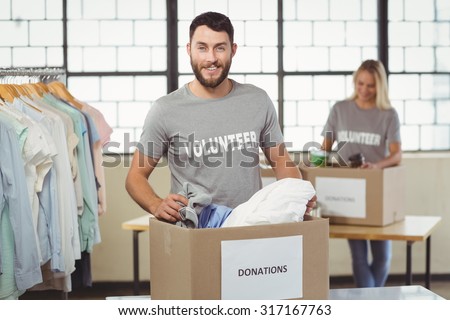 Portrait of smiling volunteer separating clothes from donation box in creative office
