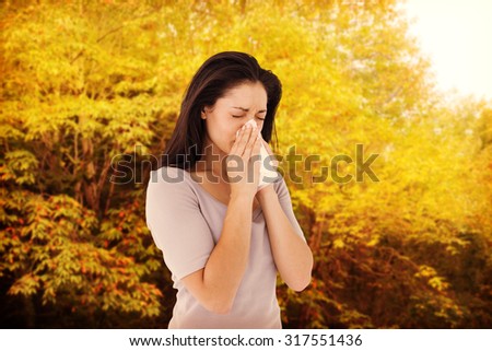 Sick brunette blowing her nose against peaceful autumn scene in forest