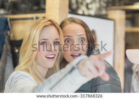 Two astonished female friends pointing away in clothes store