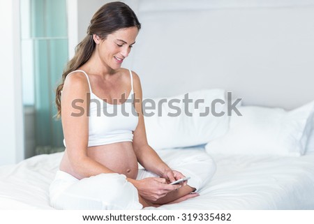 Happy woman text messaging on smartphone sitting on bed