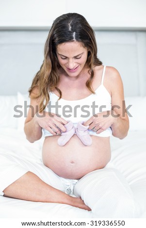 Happy woman with baby shoes on pregnant belly sitting on bed