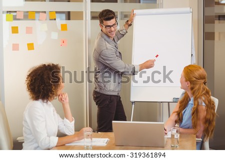 Smiling businessman discussing with female colleagues using whiteboard in office during meeting