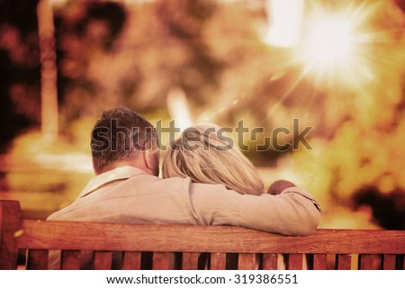 Elderly couple sitting on the bench with their back to the camera against light beam