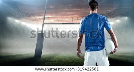 Rear view of rugby player holding ball aside against rugby stadium