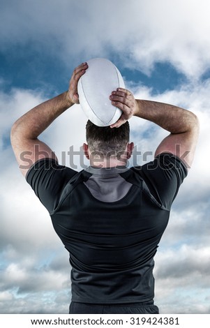 Tough rugby player throwing ball against bright blue sky with clouds