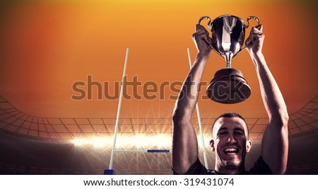 Portrait of successful rugby player holding trophy against rugby stadium