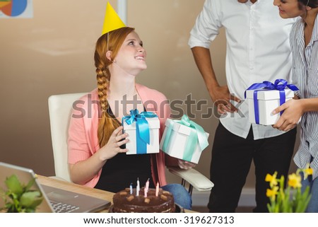 Smiling businesswoman receiving birthday gifts from colleagues in office