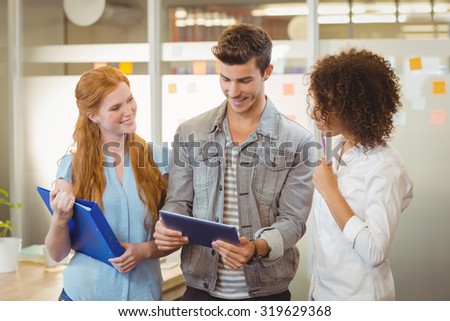 Smiling businessman using digital table while female colleagues looking at him in office