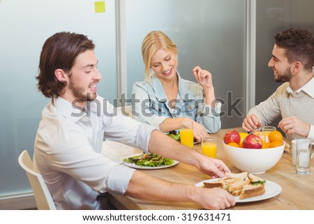 Businessman holding plate of sandwich as colleagues talking to each other during lunch in creative office