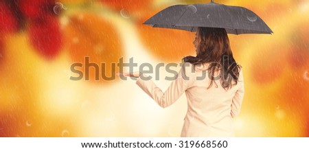 Elegant businesswoman holding black umbrella against golden leaves