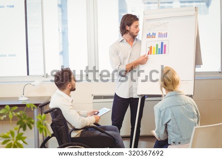 Businessman explaining multi colored graph on whiteboard while colleagues looking at it in meeting room in creative office