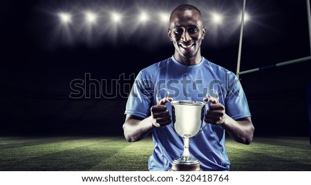 Portrait of happy athlete holding trophy against rugby stadium