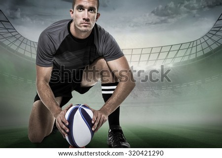 Portrait of rugby player in black jersey placing ball against rugby stadium