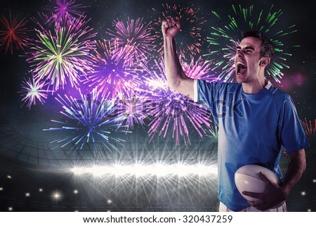 A rugby player gesturing victory against fireworks exploding over football stadium