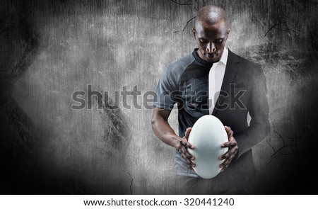 Thoughtful athlete looking at rugby ball against half a suit