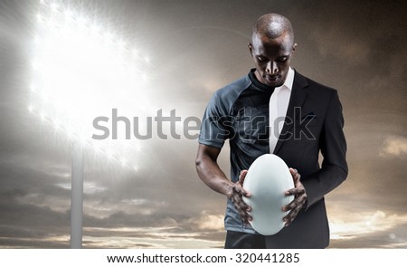Thoughtful athlete looking at rugby ball against spotlight in sky