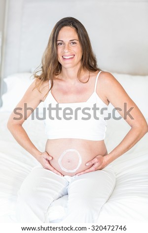 Portrait of circle moisturizer on pregnant belly sitting on bed
