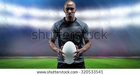 Portrait of serious athlete holding rugby ball against rugby stadium