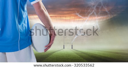 Serious rugby player with arms crossed against rugby pitch