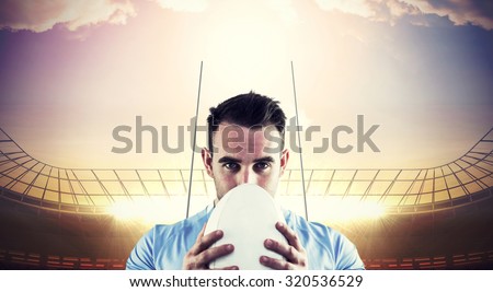 Rugby player looking at camera with ball against rugby stadium