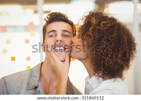 Woman with curly hair kissing shocked businessman in creative office