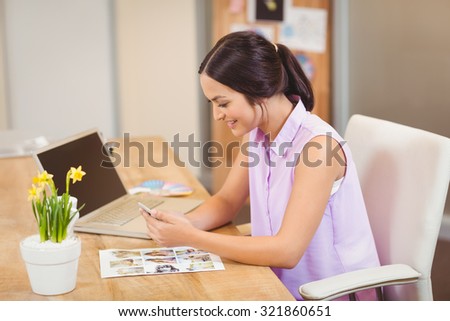 Happy businesswoman using phone on desk in creative office