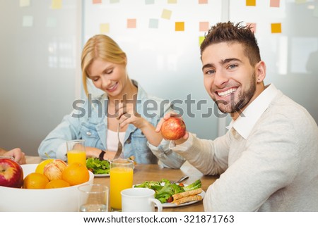Portrait of smiling employee with female colleague having breakfast in creative office