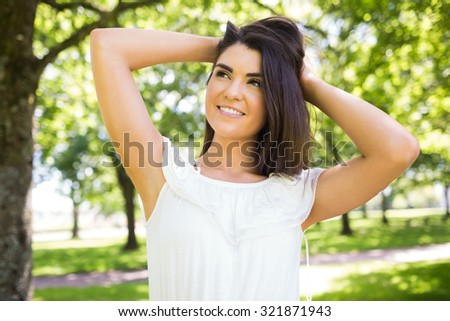Portrait of young thoughtful woman with hand in hair standing on grassland in park