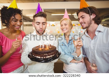 Businessman blowing birthday candles while colleagues looking at her in creative office
