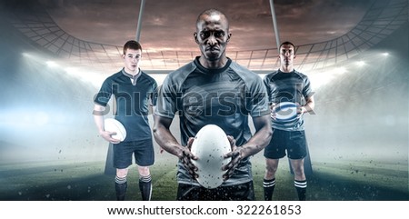 Serious rugby player in black jersey holding ball against rugby stadium