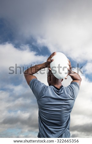 Rear view of sportsman throwing rugby ball against bright blue sky with clouds