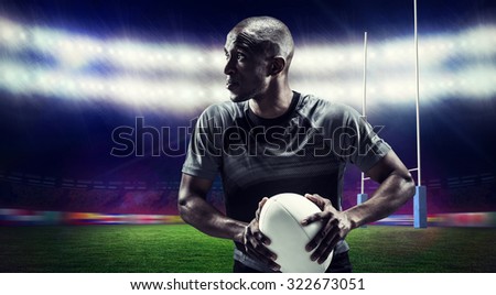 Determined rugby player holding ball against rugby stadium