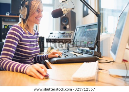 Happy female radio host using computer while broadcasting in studio