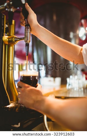 Cropped hand of bartender holding glass below beer dispenser tap at bar counter