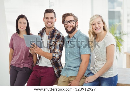 Portrait of smiling business people holding digital tablet while standing at desk in office