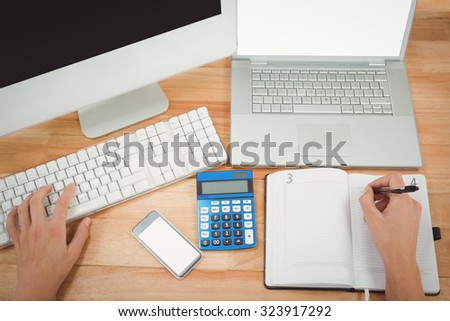 Cropped image of businessman writing on diary while using computer at desk in office