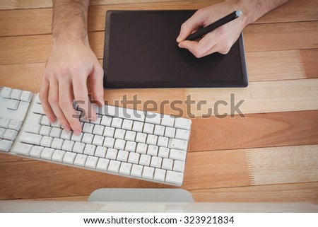 High angle view of man with graphics tablet typing on keyboard at desk in office