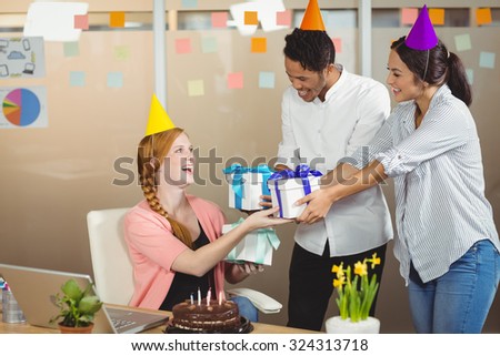 Smiling colleagues giving birthday gifts to businesswoman in office