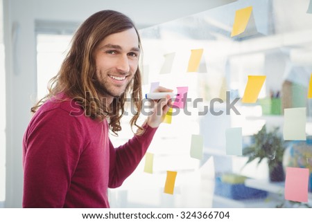 Portrait of hipster writing on sticky note stuck on glass in office