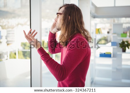 Side view of hipster talking on cellphone standing by window in office