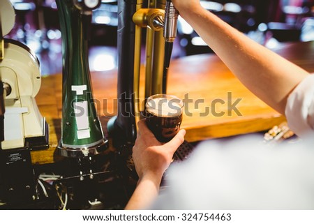 High angle view of barkeeper holding glass below beer dispenser tap at bar counter