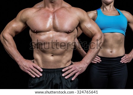 Midsection of muscular man and woman standing with hands on hip against black background