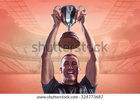 Portrait of successful rugby player holding trophy against orange
