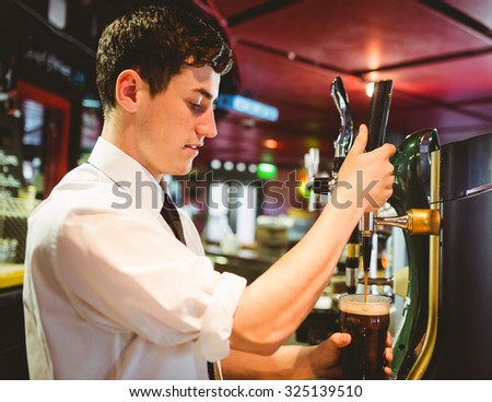Barkeeper holding beer glass below dispenser tap at bar counter