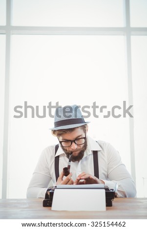 Hipster smoking pipe while working at desk against window in office