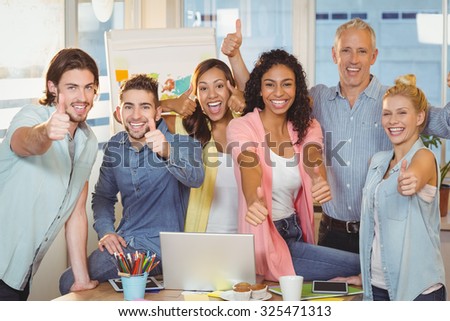 Portrait of happy business people with technologies showing thumbs up in creative office